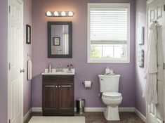 a bathroom with a toilet, sink and mirror in it's center wall color is purple