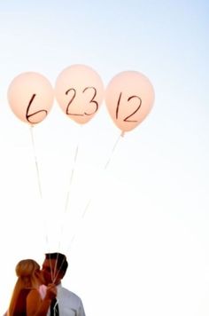 a couple kissing while holding balloons with the numbers 1232 written on them in black