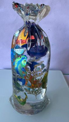 a clear glass vase with colorful fish and plants in it on top of a table