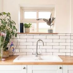 a kitchen with white cabinets and wooden counter tops, plants in vases on the window sill