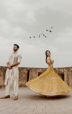 a man and woman standing next to each other in front of birds flying above them