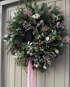 a wreath hanging on the side of a door with pink ribbon and flowers around it