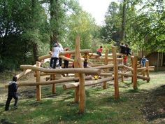 children playing on a wooden play structure in the park with people standing around and looking at it