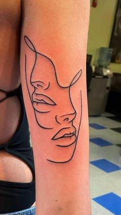 a woman's arm with a tattoo on it that has a line drawing of a mask