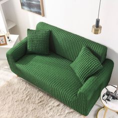 a green couch sitting on top of a white rug next to a table and lamp