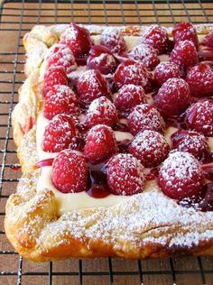 a pastry covered in powdered sugar and raspberries on a wire cooling rack