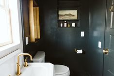 a white toilet sitting next to a bathroom sink under a window in a black wall