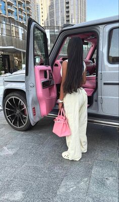 a woman standing in the open door of a car with her pink handbag and purse