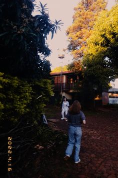 two people are playing frisbee in the yard near some trees and bushes on a sunny day