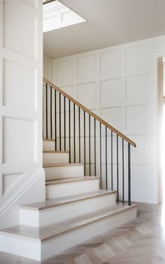 a white staircase with black railing and wooden handrail in an empty room, looking into the doorway