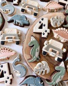 decorated cookies with cars and dinosaurs are arranged on a wooden platter in the shape of numbers