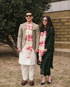 a man and woman standing next to each other in front of a tree with flowers on it