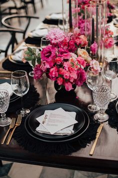 the table is set with black and white plates, silverware, and pink flowers