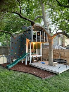 a backyard with a tree, swing set and climbing wall in the back yard area