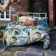 a bed sitting on top of a stone floor next to a brick wall and tree