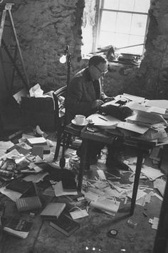 a man sitting at a desk with lots of papers on the floor in front of him