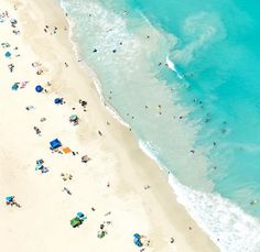 an aerial view of people on the beach and in the water at the ocean's edge