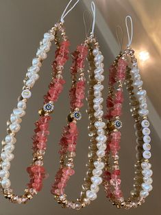 three necklaces hanging from the ceiling with pearls and other beads on each bead