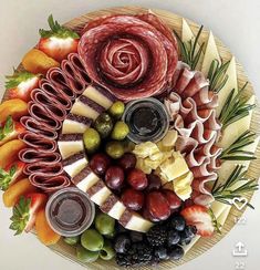 a platter filled with meats, cheeses and fruit on top of a table