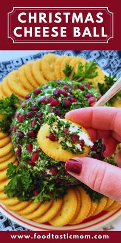 christmas cheese ball with pomegranates and herbs on top is being held up by a woman's hand