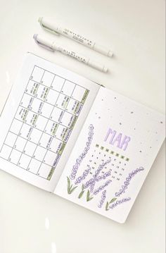 an open planner with lavender flowers on it next to two markers and a marker pen