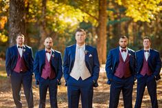 a group of men standing next to each other in front of trees and leaves on the ground