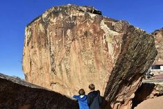 two boys standing next to a large rock