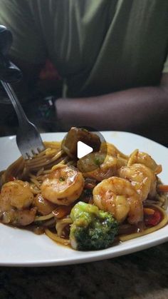 a plate with shrimp, broccoli and noodles on it next to a man