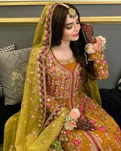 a woman in a yellow and pink bridal outfit sitting on a couch with her hands behind her head