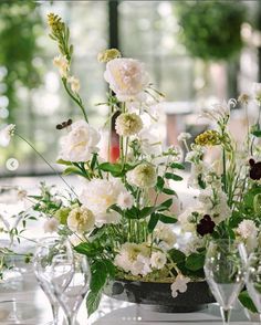 white flowers are arranged in vases on a table with wine glasses and silverware