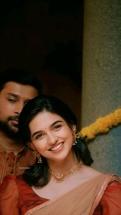 a man standing next to a woman in a red and beige sari smiling at the camera