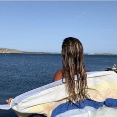 a woman sitting on the back of a boat with a towel over her head looking out to sea