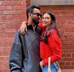 a man and woman standing next to each other in front of a brick wall