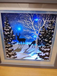 a framed paper art depicting two deer in the woods at night with stars and snow