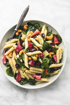 a white bowl filled with pasta, strawberries and spinach on top of a marble table