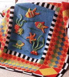 a crocheted blanket with fish and seaweeds on it, sitting on the floor