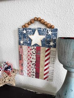 an american flag wall hanging on the side of a white wall next to a vase