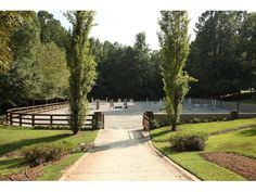 an empty path leading to a horse stable with trees in the foreground and fencing on either side