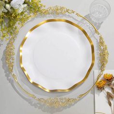 a white plate with gold trim around the edge and some flowers on the table next to it