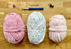 three balls of yarn are sitting on a wooden surface next to a crochet hook