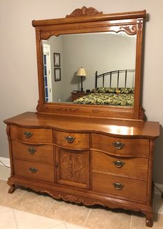 a bedroom scene with focus on the dresser and bed in the background, there is a large mirror over the dresser