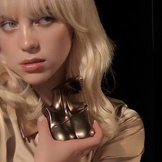 a woman with blonde hair and blue eyes holding a gold object in her right hand