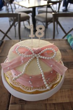 a birthday cake decorated with pearls and pink ribbon on a table in a restaurant or cafe