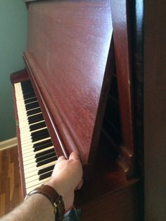 a person is playing the piano with their hand on it's keys and leaning up against an upright wooden case