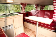 the interior of a camper with red and white checkered curtains, wood flooring, and table