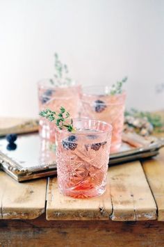 three glasses filled with blueberries and mint sprigs on top of a wooden tray