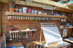 an artist's easel in front of a brick wall with lots of tools hanging on it