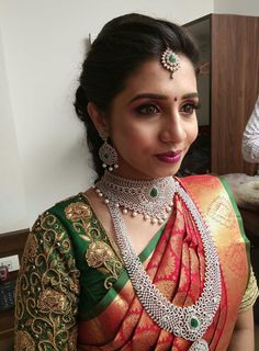 a woman in a green and red saree with jewelry on her neck, smiling at the camera