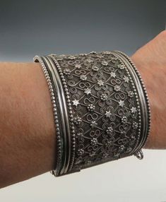 Presented is a unique hand made silver filigree cuff bracelet. It may be a piece of Berber, Bedouin, or other north African tribal silver work, or it may be Indian or otherwise southeast Asian, it is difficult to say based on style alone, though I've seen Indian wedding jewelry with a very similar look. The bracelet is made as a 2 inch wide band, hinged and with a pin 'lock' clasp, so it will be very secure when worn. The design is quite intricate, made up of applied filigree wirework in a lattice pattern, with little spirals, florettes, and stars in alternating rows. It's a very well made piece, with a great feeling of weight and quality on the wrist.   This piece is not stamped or hallmarked that we could find, but we have tested it with nitric acid and guarantee it to be about 900 purit Traditional Metal Cuff Bracelet With Intricate Design, Antique Silver Oxidized Cuff Bracelet, Bohemian Silver Cuff Bracelet With Intricate Design, Oxidized Cuff Bracelet For Ceremonial Festivals, Traditional Oxidized Cuff Bracelet, Lattice Pattern, Indian Wedding Jewelry, Wide Cuff, Oxidised Jewellery