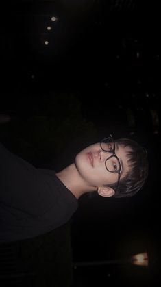 a woman with glasses is staring into the distance at night in front of some lights